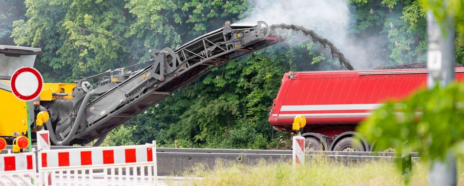 Asphalt milling and grinding machine at road repair and construction site throwing shredded old bitumen in big industrial heavy dumper tipper truck for recycling.