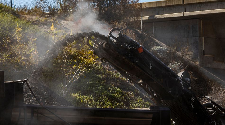 Close up of hot steaming asphalt pouring off of the conveyor belt of an asphalt milling machine