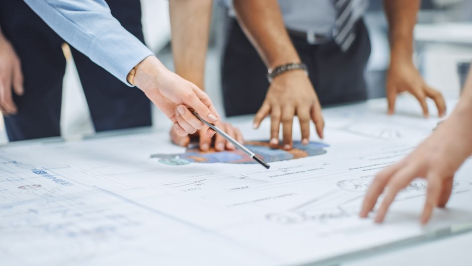 Close-up on Hands of Group of Engineers, Technicians and Specialists on a Meeting, Tracing Lines and Analysing Engine Design Technical Drafts Laying on the Table