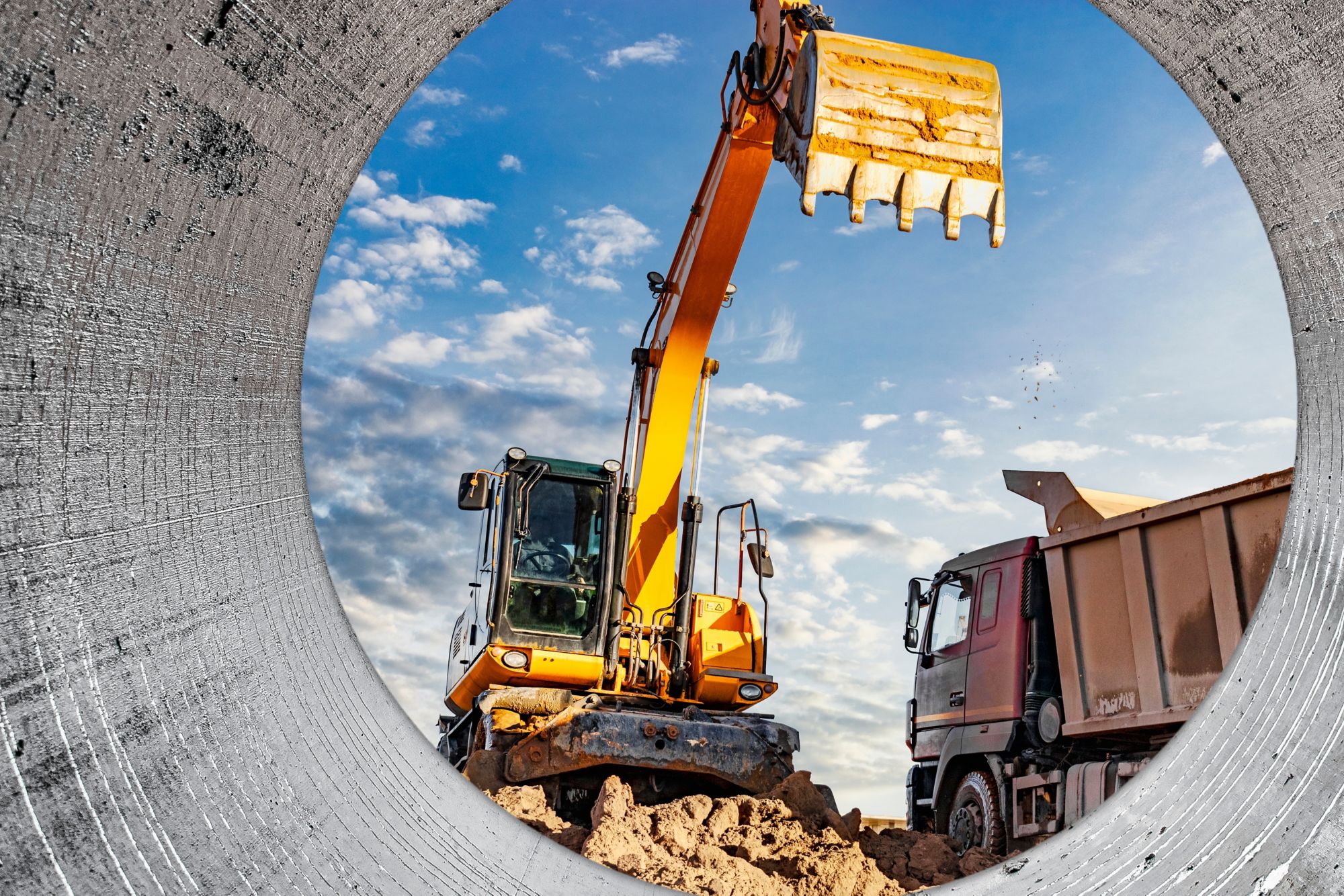 A wheeled excavator loads a dump truck with soil and sand. An excavator with a high-raised bucket against a cloudy sky View from the trench. Removal of soil from a construction site.